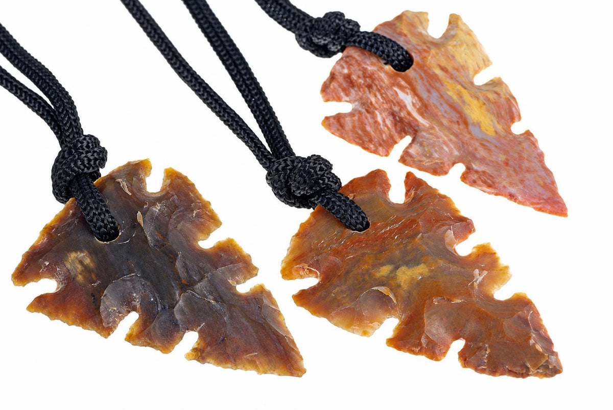 Three jasper arrowhead pendants show brown, orange and reddish patterns, with notched edges and knotted black cords on a white background.