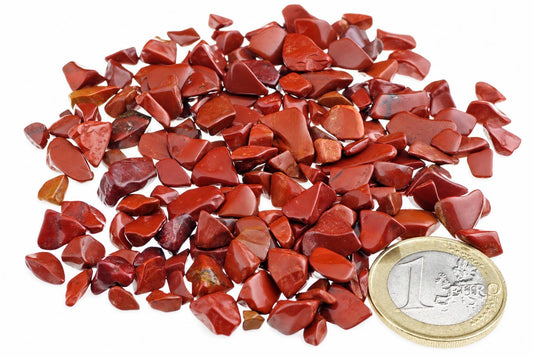 A pile of small, polished red jasper stones on a white surface with a one euro coin for scale.