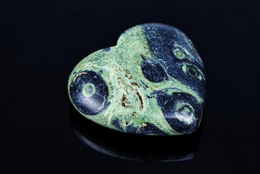A polished heart-shaped stone with green and dark blue swirls, resting on a dark surface.