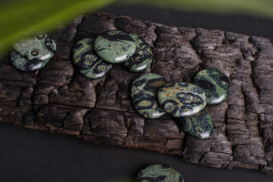 Several polished green and black patterned stones rest on a dark, textured wooden surface.