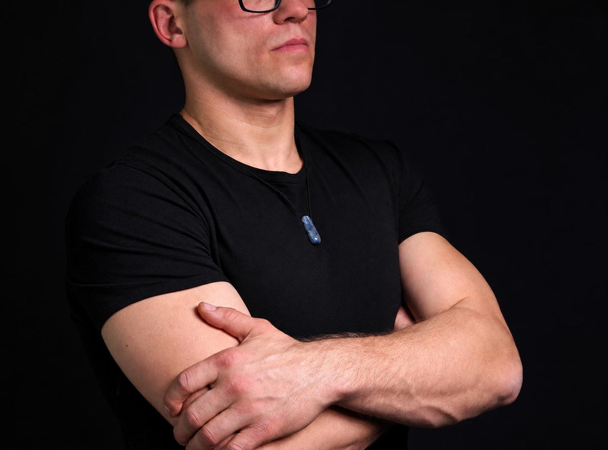 A man in a black t-shirt wears a blue pendant on a dark surface.