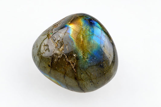 A rounded grey-green stone shows blue and golden iridescence, dark inclusions and fine lines on white.
