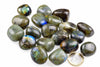 Polished grey and olive stones with blue and green flashes are grouped on a white background beside a one-euro coin.