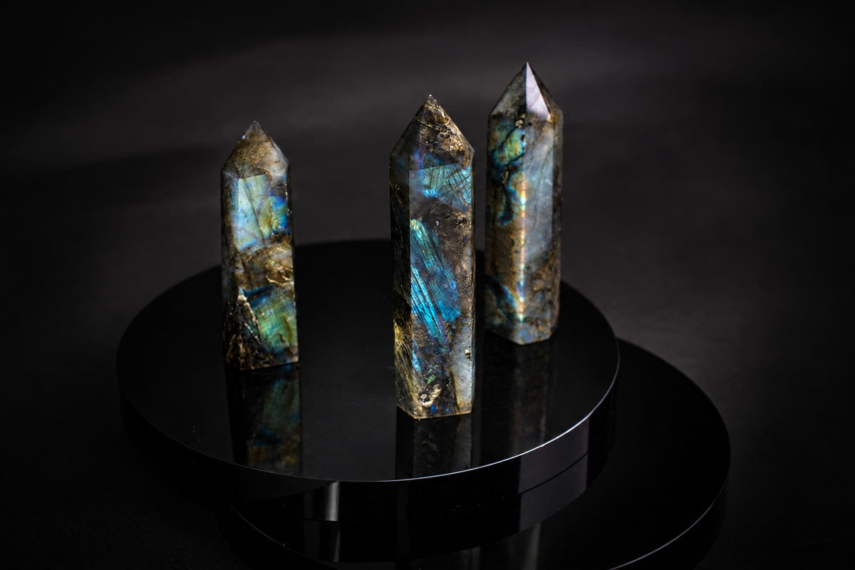 Three pointed labradorite towers with blue and gold-colored flashes stand upright on a black circular display against a dark background.