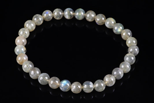 A bracelet of pale grey translucent round beads with subtle blue-green flashes forms a circle on black.