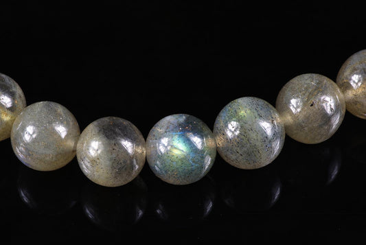 Close-up of pale grey round beads with dark speckles and blue-green flashes on a glossy black surface.