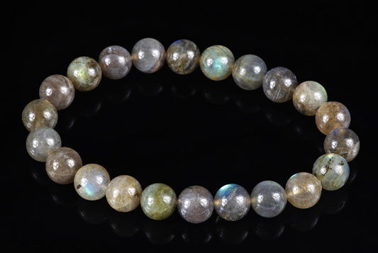 A bracelet of round beads with grey, brown and blue iridescent Labradorite on a dark surface.