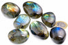 Seven smooth grey-green stones with blue, green and golden iridescent flashes rest beside a euro coin.