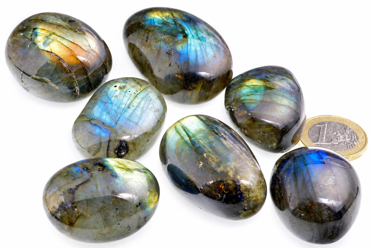 Seven smooth grey-green stones with blue, green and golden iridescent flashes rest beside a euro coin.
