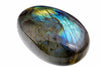 A smooth oval grey-green stone shows a broad blue-green and golden sheen with fine dark lines on white.