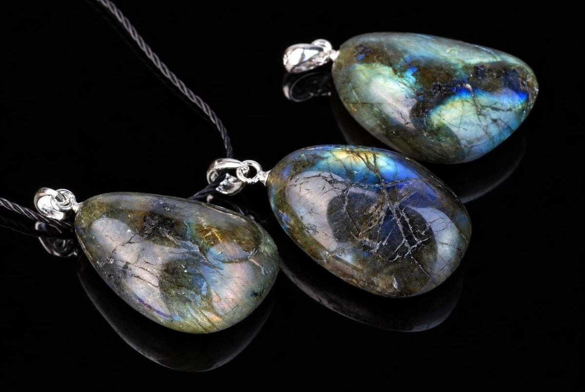 Three teardrop-shaped labradorite pendants with silver-toned settings on dark cords, resting on a black reflective surface.