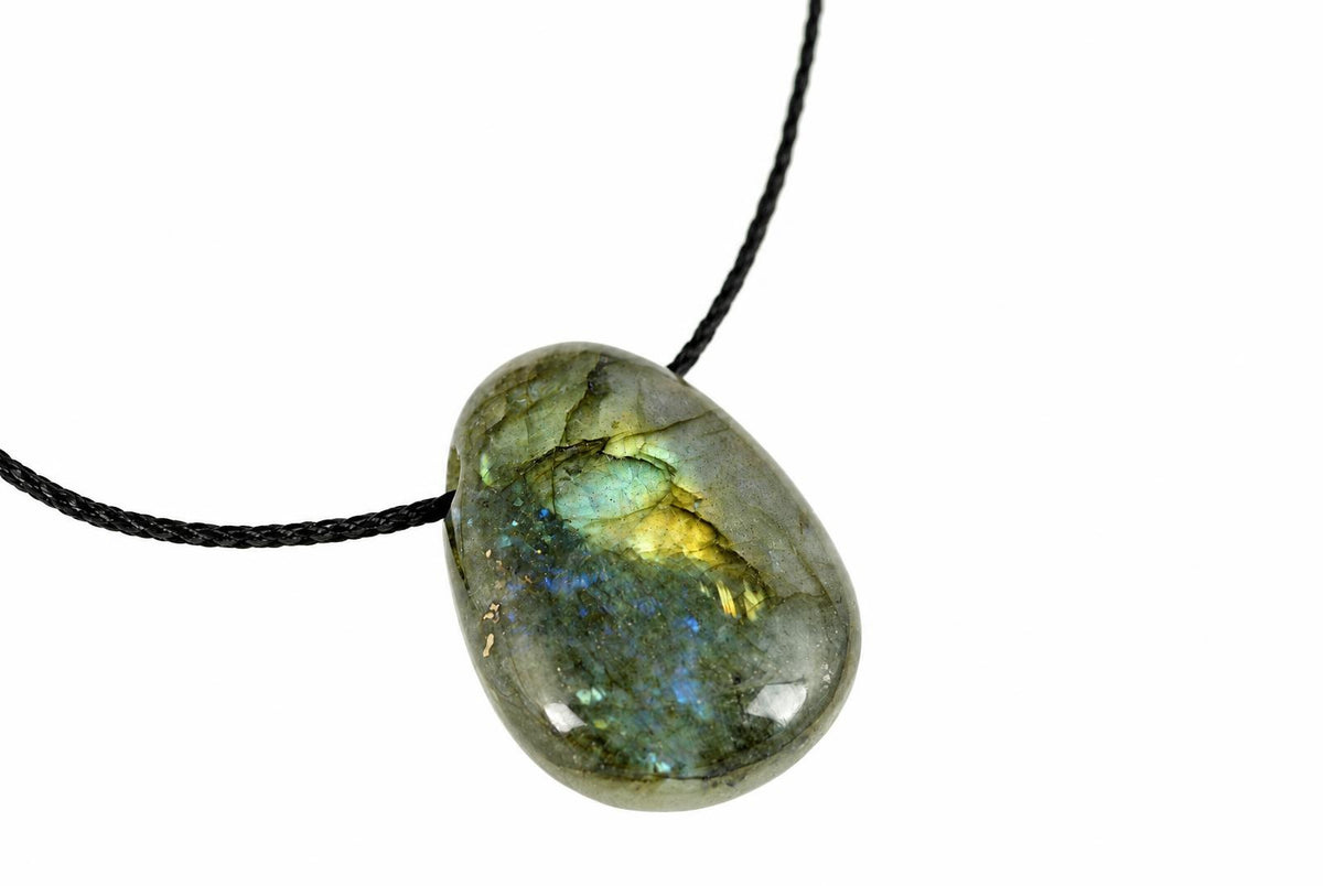 A polished oval labradorite pendant with blue, green and yellow flashes hangs from a black cord against a white background.