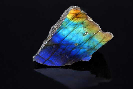 An irregular stone slab shows deep blue, bright blue, green and golden sheen across its face on a black surface.