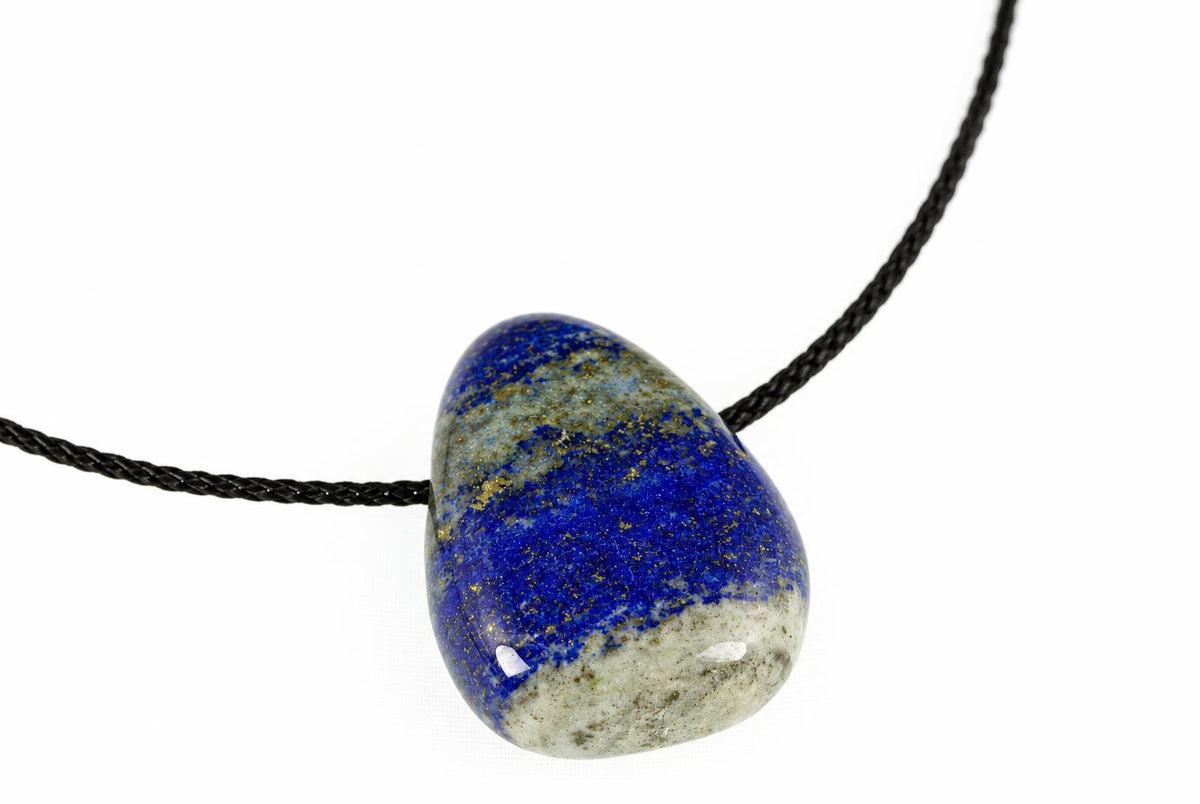 A polished lapis lazuli drop pendant has deep blue colouring and broad pale bands, hanging from a black cord against white.