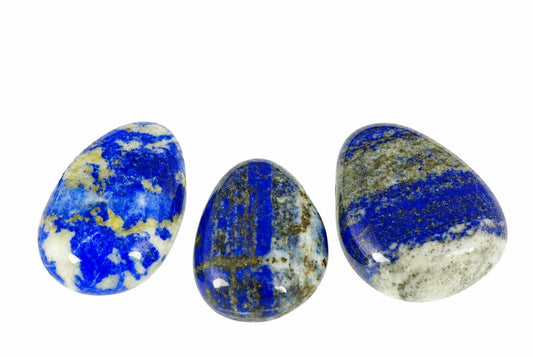 Three polished, teardrop-shaped stones with deep blue, white and gold-coloured patterns on a pale surface.