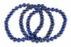 Overlapping bracelets of glossy deep-blue round beads with pale and gold-toned flecks lie on white.