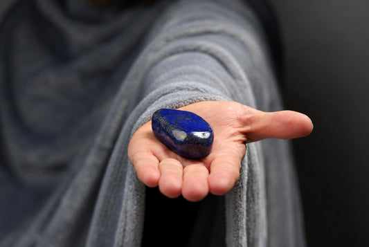 A hand holds a polished, deep blue stone with golden flecks on a dark surface.