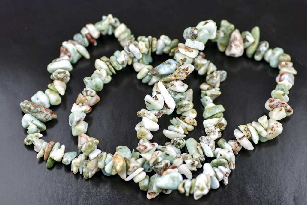 A Larimar bracelet made of irregular chips in pale green, white and brown tones arranged on a dark surface.