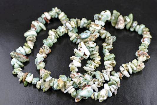 A Larimar bracelet made of irregular chips in pale green, white and brown tones arranged on a dark surface.