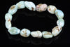 A Larimar bracelet with smooth, rounded beads in pale blue and white tones, some with brown or pinkish spots, arranged on a dark reflective surface.