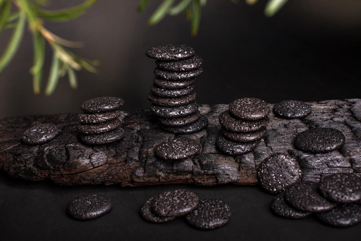 Stacks of dark, porous palmstones arranged on a weathered wooden surface with green foliage in the background.
