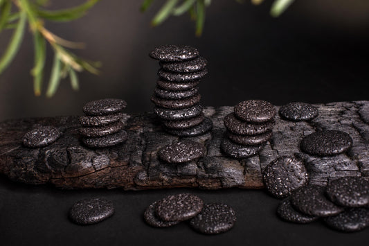 Stacks of dark, porous palmstones arranged on a weathered wooden surface with green foliage in the background.
