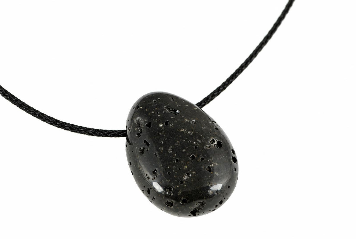 A black lava stone pendant with a smooth, rounded shape and small holes on its surface hangs from a dark cord against a white background.