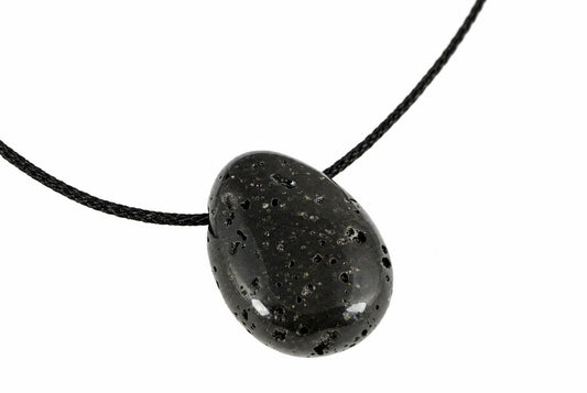 A black lava stone pendant with a smooth, rounded shape and small holes on its surface hangs from a dark cord against a white background.