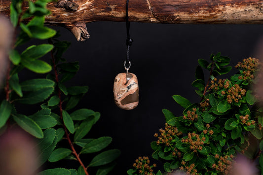 A polished, oval-shaped pendant with swirling brown and cream patterns hangs from a black cord against a dark background.