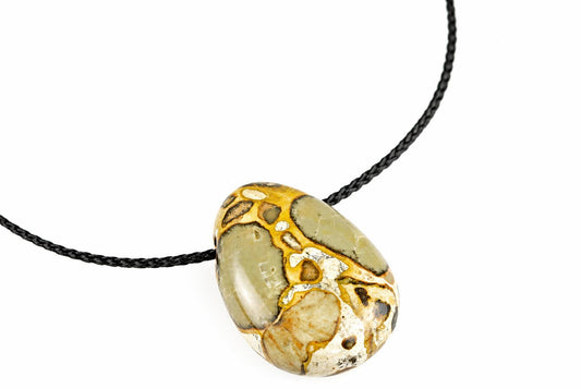 A polished oval pendant with green, cream and gold-coloured patterns hangs on a black cord against a white background.