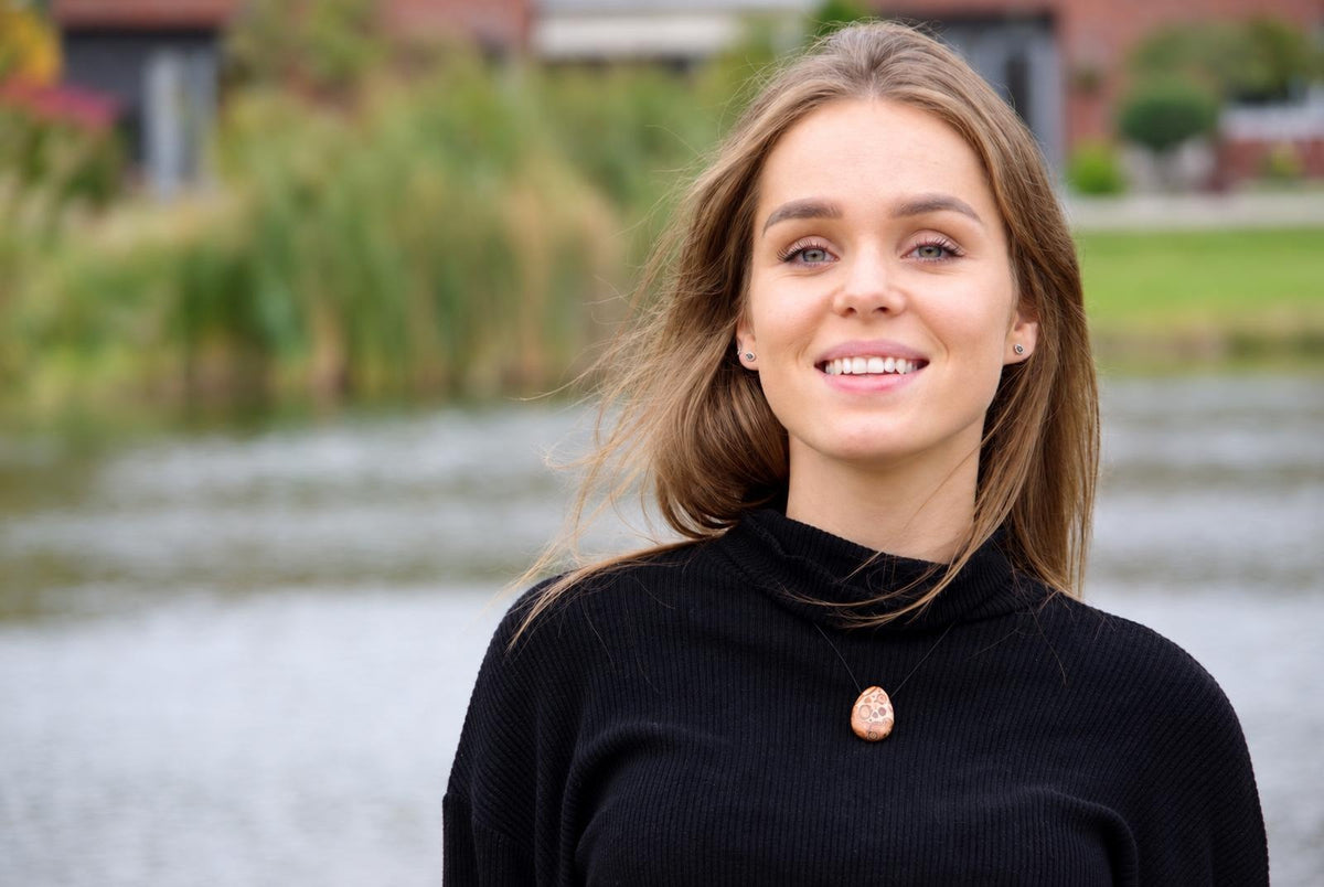 A woman wears a black turtleneck sweater with a brown, oval pendant featuring light spots on a dark cord.
