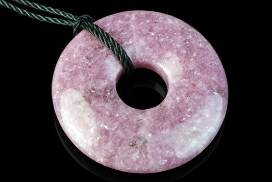 A pink and white speckled donut-shaped pendant with a central hole, threaded on a dark green cord against a black background.