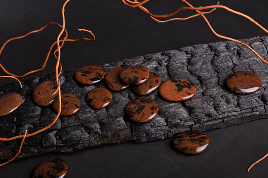 Polished reddish-brown palmstones with black patches are scattered over textured wood and a dark surface among thin dried stems.