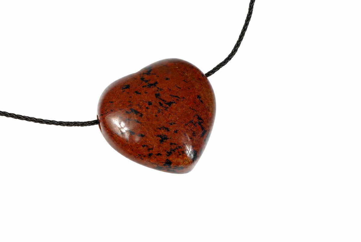 A heart-shaped pendant with a polished reddish-brown stone and black speckles hangs on a dark cord against a white background.