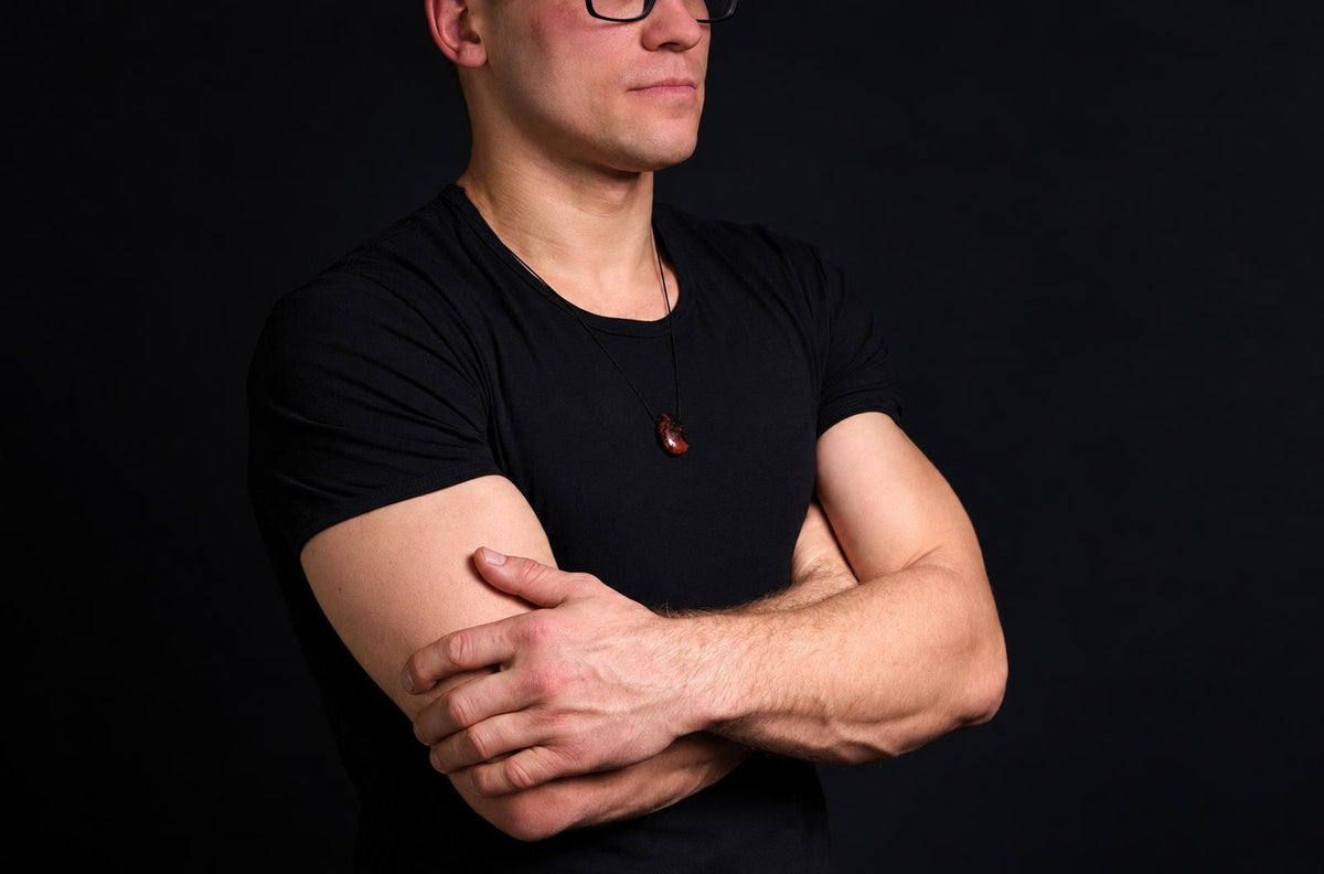 A man in a black t-shirt wears a dark reddish-brown pendant on a thin cord against a dark background.