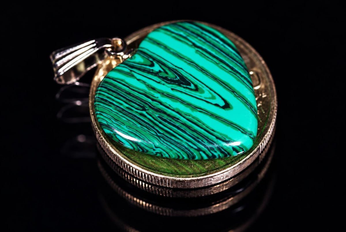 A heart-shaped pendant with a green and black swirled stone set in a silver-toned metal frame on a dark reflective surface.