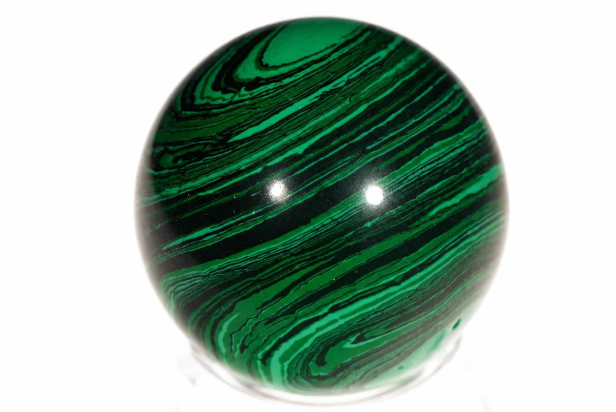 A polished sphere with swirling green and black bands, resting on a clear stand against a white background.