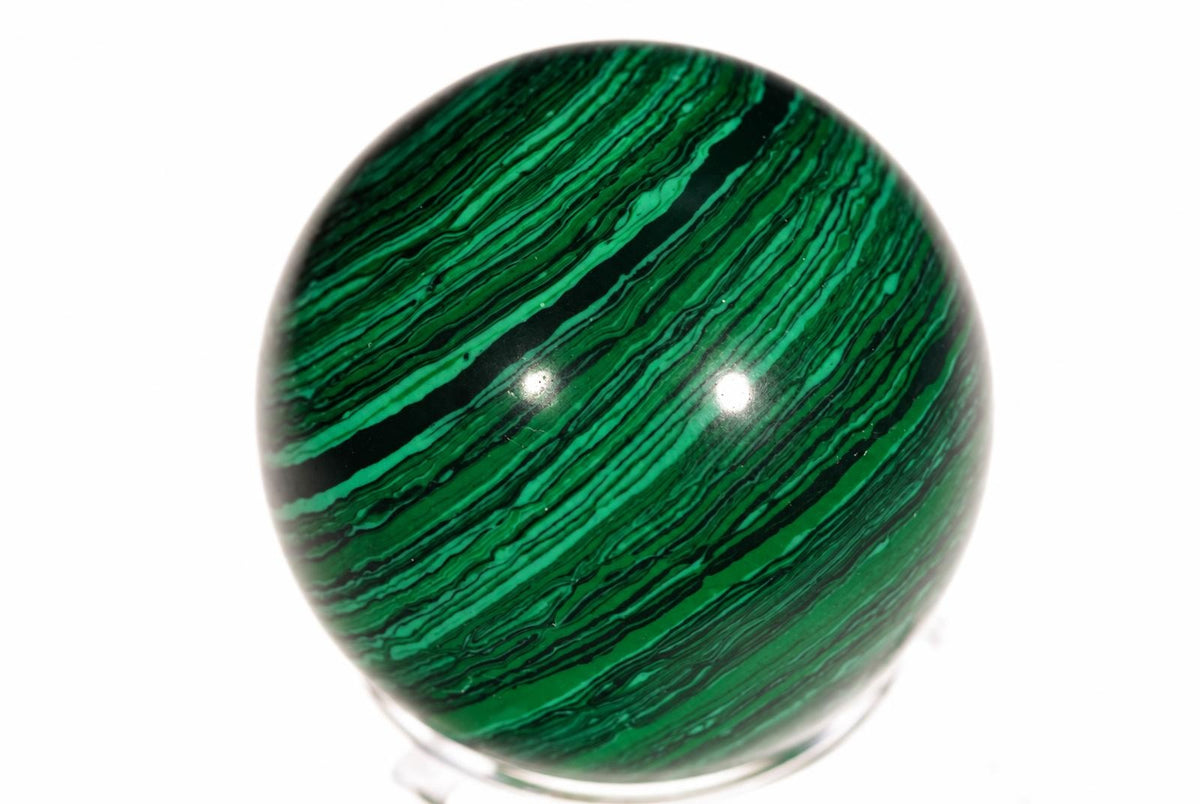 A polished green sphere with dark wavy stripes sits on a clear stand against a white background.