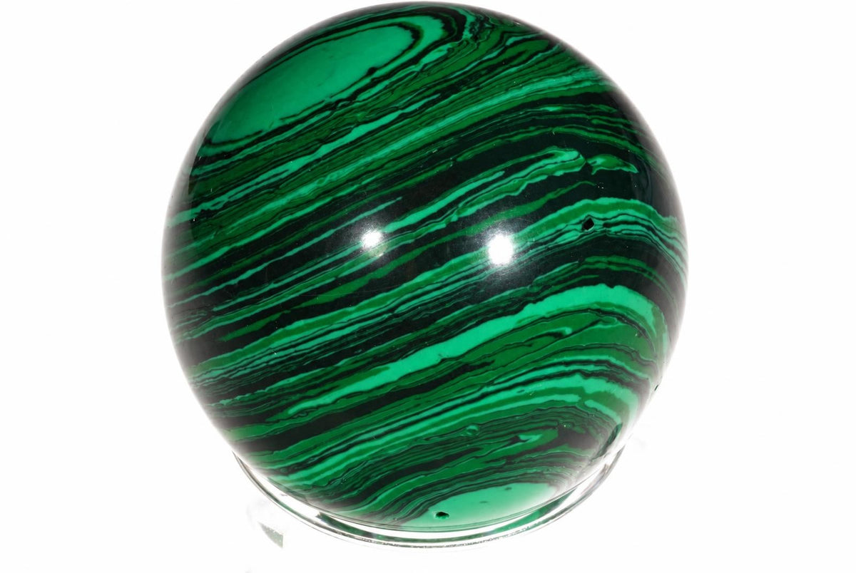 A polished sphere with swirling green and black bands, resting on a clear stand against a white background.