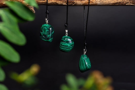 Three polished green stone pendants with darker bands hang from black cords beneath a branch against a dark background.