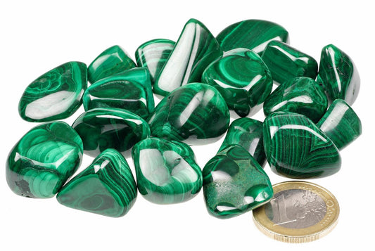 A pile of polished green malachite stones with white banding, arranged on a pale surface next to a one-euro coin.