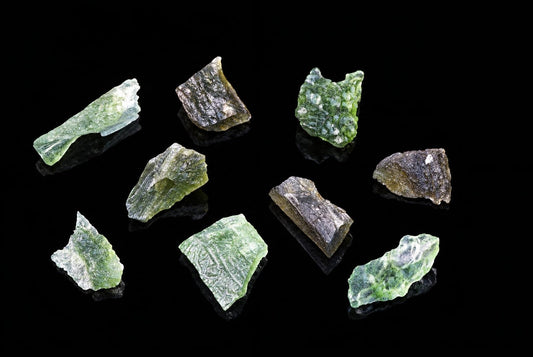 Several pieces of green, bubbly Moldavite crystals are arranged on a dark, reflective surface.