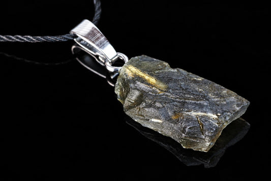 A dark green, rough-textured pendant with golden inclusions hangs from a silver-toned bail on a black cord against a dark surface.