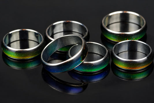 Six metallic rings with green, blue and orange speckled bands on a dark reflective surface.