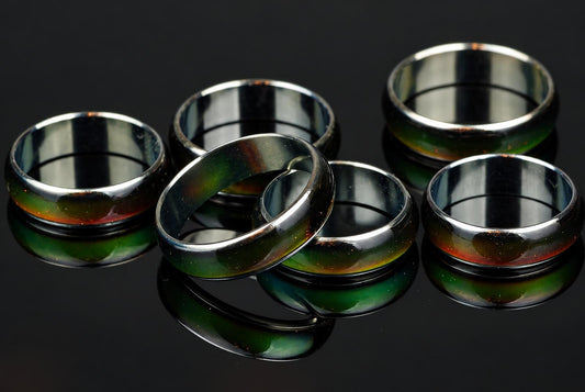 Six metallic rings with green and red iridescent bands rest on a dark, reflective surface.