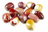 A collection of polished Mookaite Jasper stones in red, white, yellow and brown tones arranged on a pale surface.