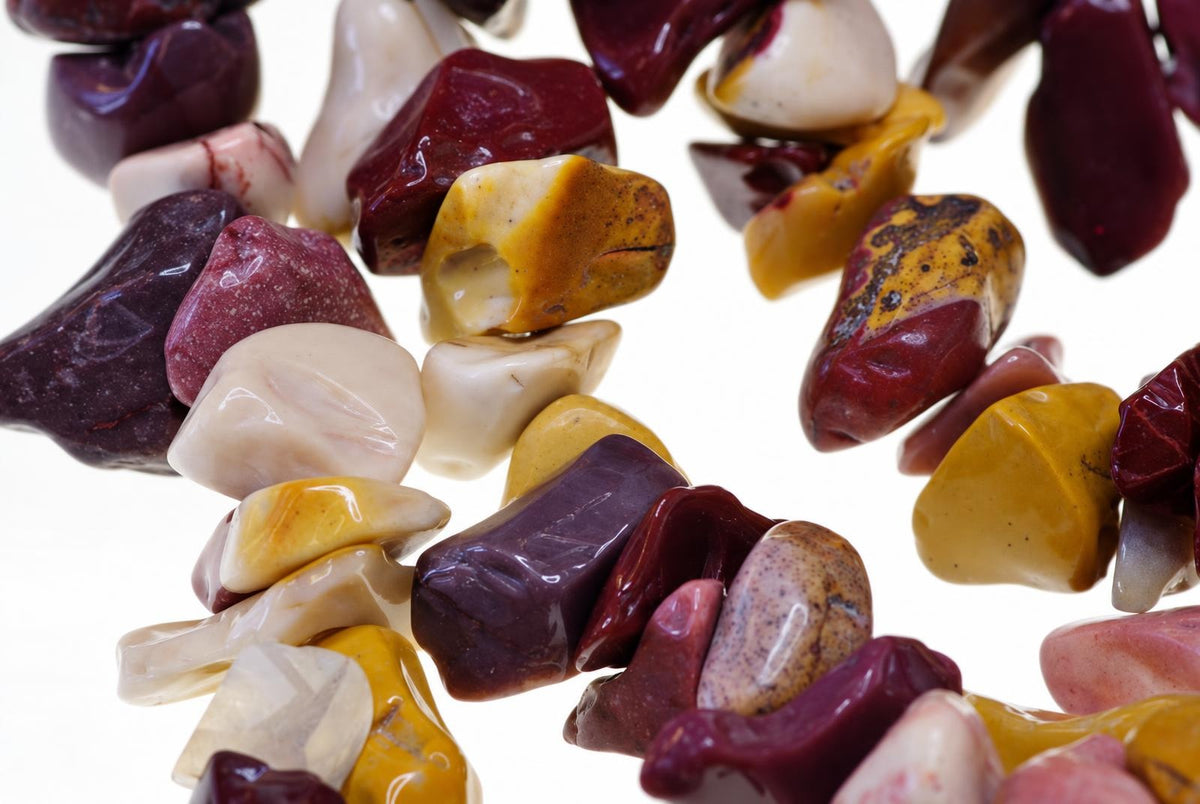 A bracelet made of polished, irregular chips in dark red, cream, yellow and brown tones on a white background.