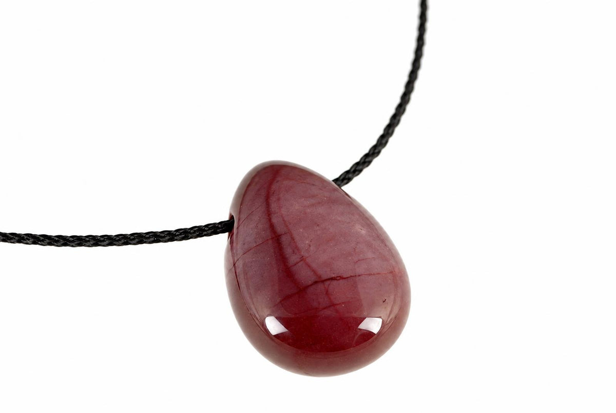 A polished, teardrop-shaped pendant in deep red with lighter veining hangs from a black cord against a white background.