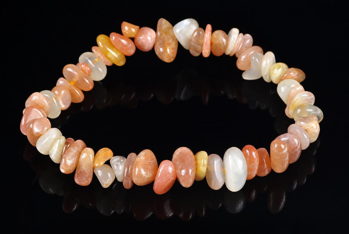 A bracelet made of smooth, polished chips in peach, cream, and pale yellow tones arranged on a dark reflective surface.
