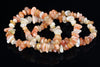 A bracelet made of smooth, polished chips in peach, cream, and pale yellow tones arranged on a dark reflective surface.